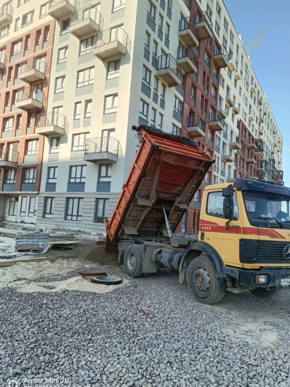 Самосвал выгружает песок на щебёночное основание жилого комплекса
